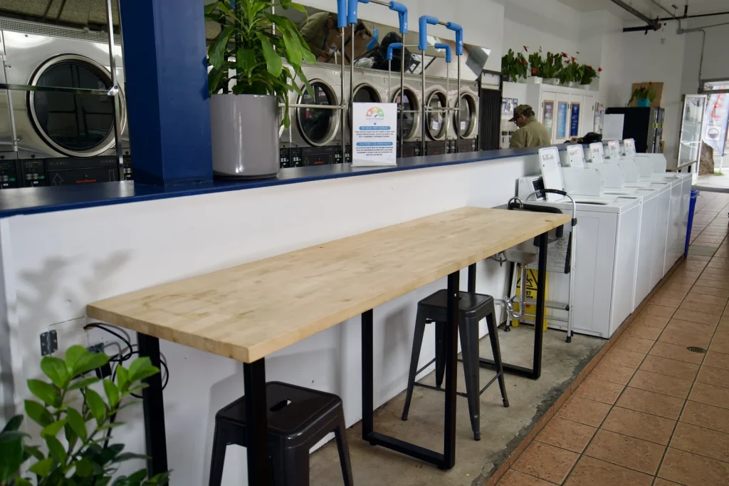 Butcher block folding counter with stools beside the machine aisle at The Laundry Hub SF