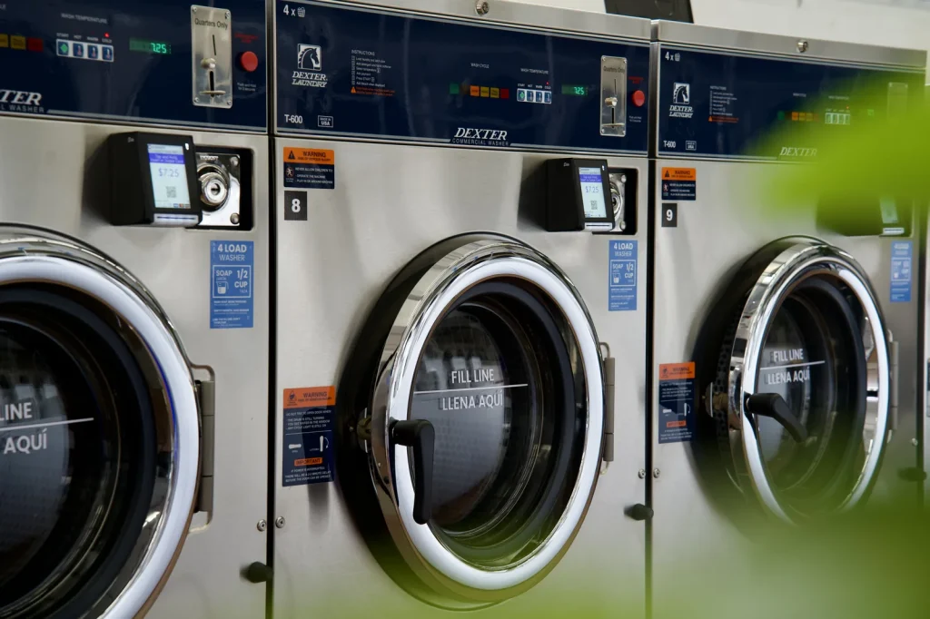 Row of Dexter washers with bilingual FILL LINE and LLENA AQUI door markings at The Laundry Hub SF